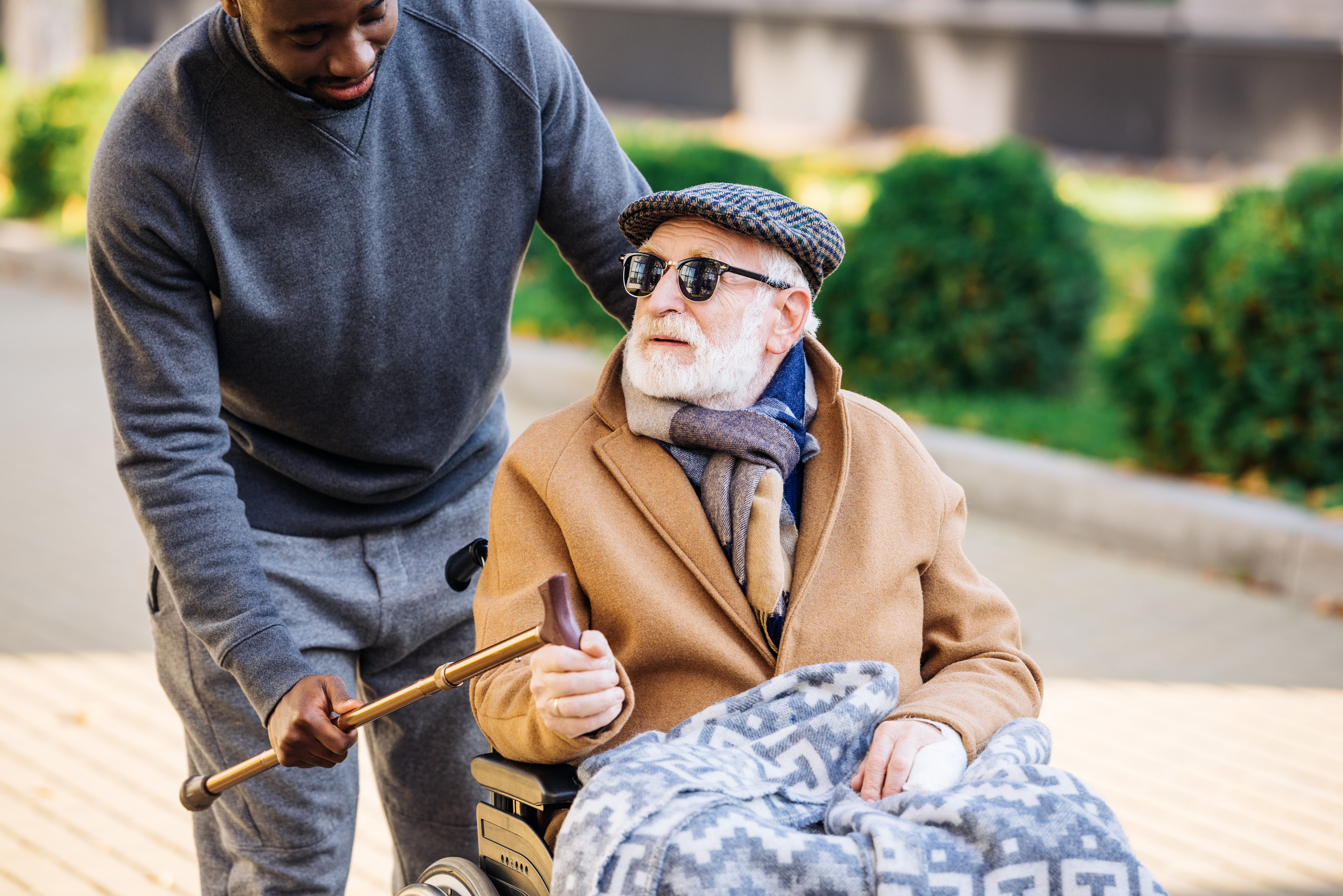 young man giving walking stick to senior disabled man in wheelchair on street