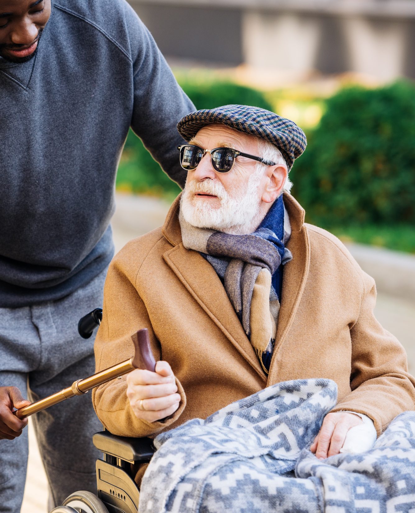 young man giving walking stick to senior disabled man in wheelchair on street